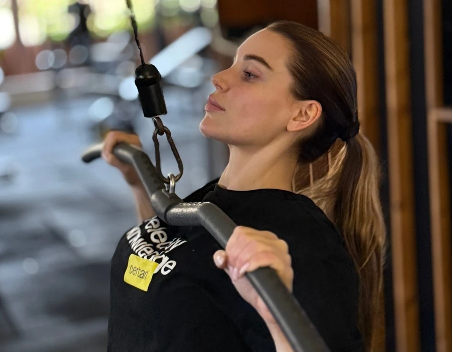 Kvinna i en Certan t-shirt som gör latsdrag på gymmet.
